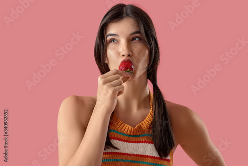 Beautiful young woman eating fresh strawberry on pink background
