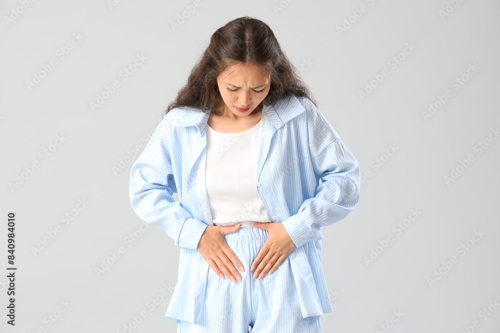 Young Asian woman suffering from menstrual cramps on light background Young Asian woman suffering from menstrual cramps on light background