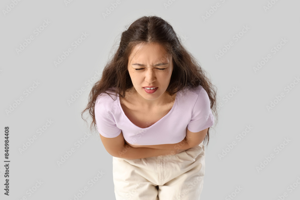 Young Asian woman suffering from menstrual pain on light background Young Asian woman suffering from menstrual pain on light background