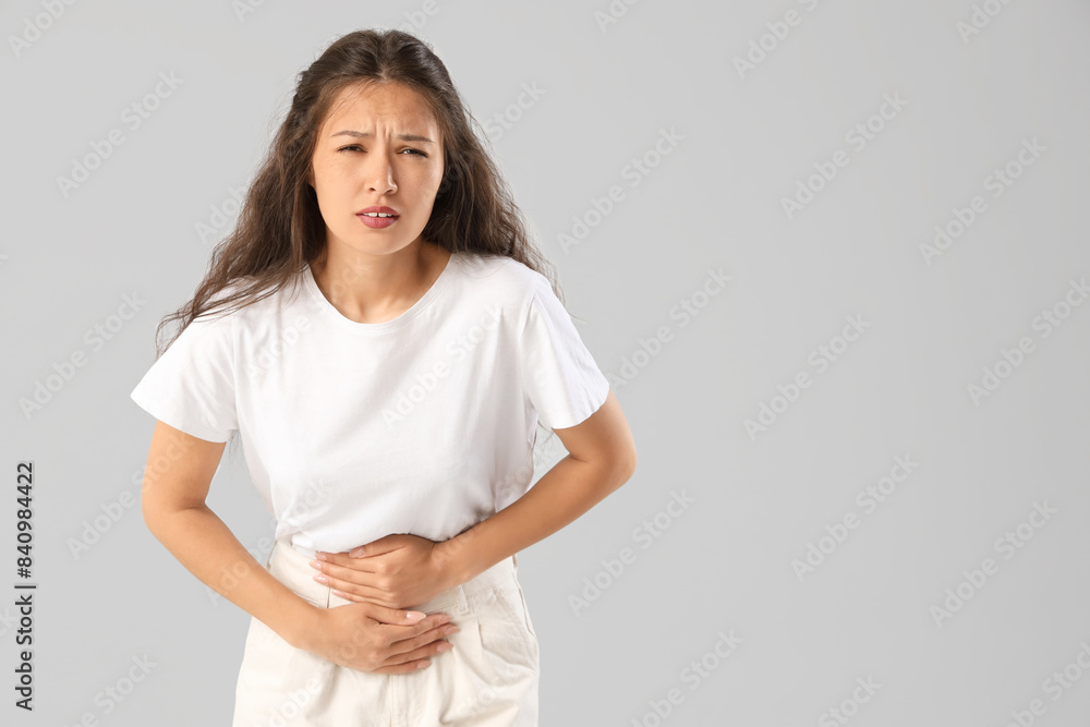 Young Asian woman suffering from menstrual pain on light background