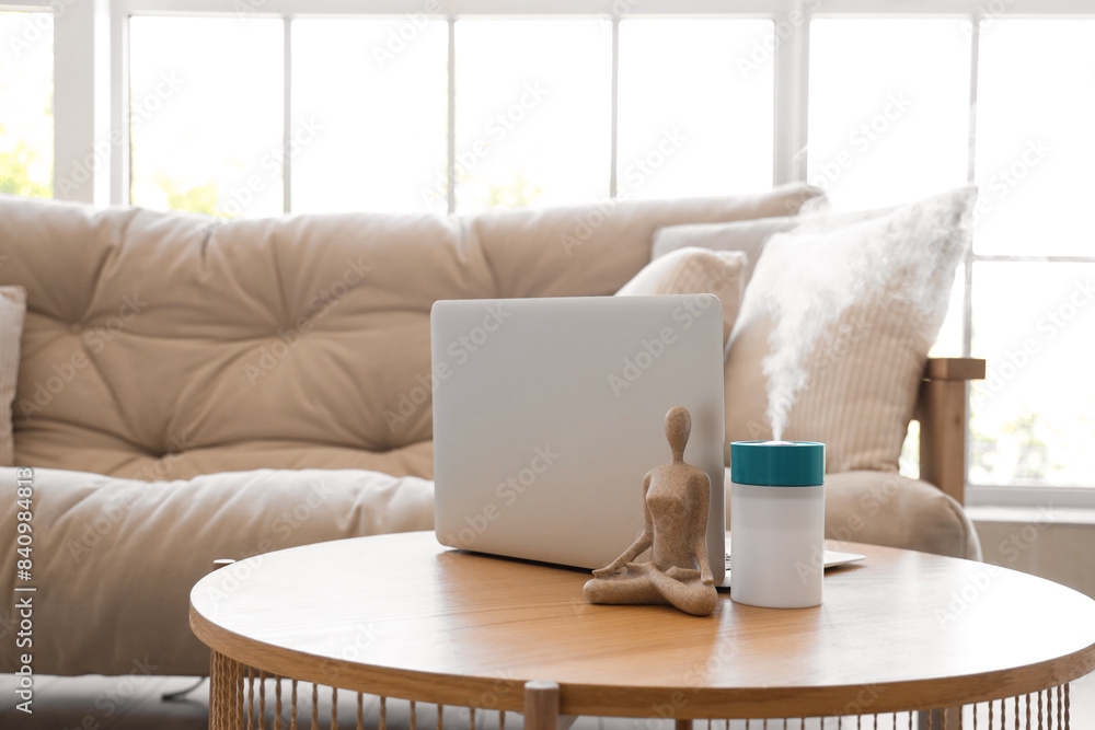 Air humidifier with statuette and laptop on table in living room, closeup Air humidifier with statuette and laptop on table in living room, closeup