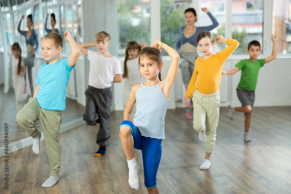 Active preteen girl practicing sport dances with other children and teacher during dancing classes