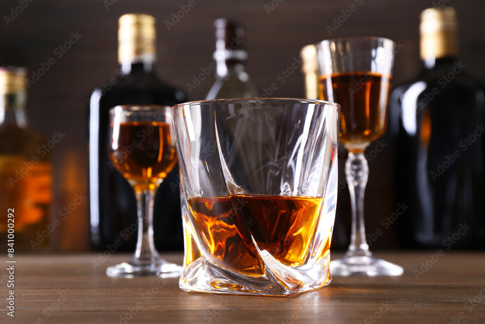 Different delicious liqueurs in glasses and bottles on wooden table, closeup Different delicious liqueurs in glasses and bottles on wooden table, closeup