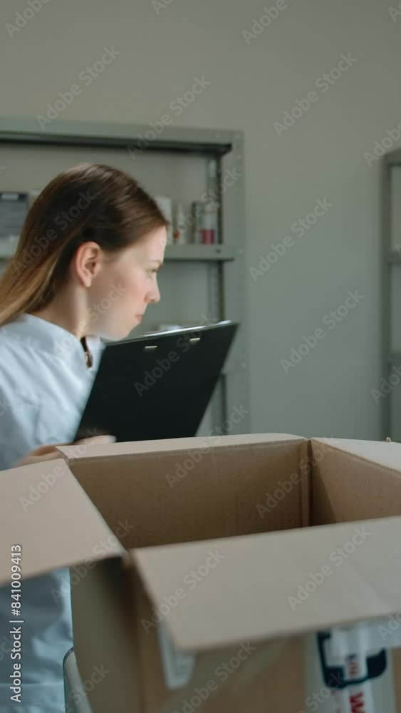 Attractive caucasian woman unpacking delivery with medicine in pharmacy. Female with text tablet checking stuff in carton box and rowing medicines on showcase shelfs. Vertical shot. Attractive caucasian woman unpacking delivery with medicine in pharmacy. Female with text tablet checking stuff in carton box and rowing medicines on showcase shelfs. Vertical shot.