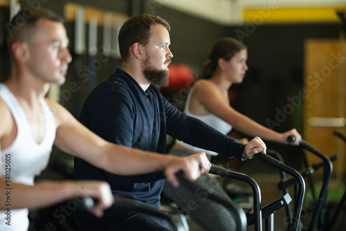 Willing young man engaged in air-bike workout in exercise room during weight training classes