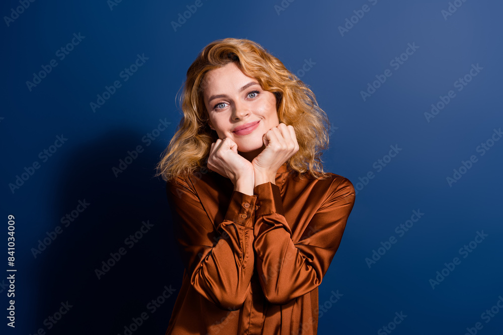 Portrait of lovely cute dreamy girl with curly hairdo wear silk blouse holding arms on chekbones isolated on dark blue color background Portrait of lovely cute dreamy girl with curly hairdo wear silk blouse holding arms on chekbones isolated on dark blue color background