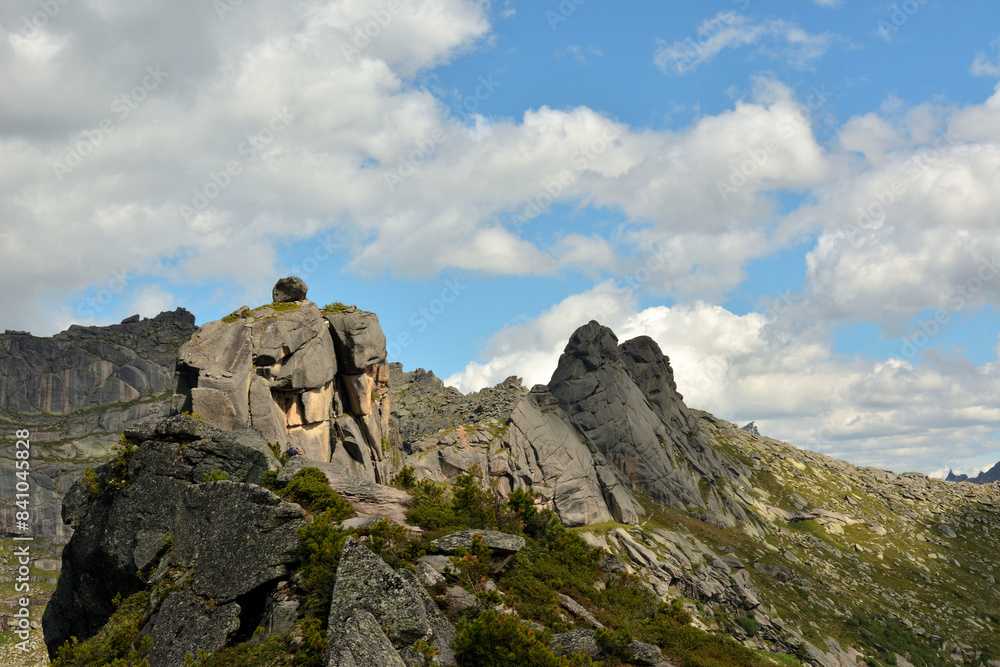 Pointed rocks of a mountain range with a round stone on top under a cloudy clear sky. Pointed rocks of a mountain range with a round stone on top under a cloudy clear sky.