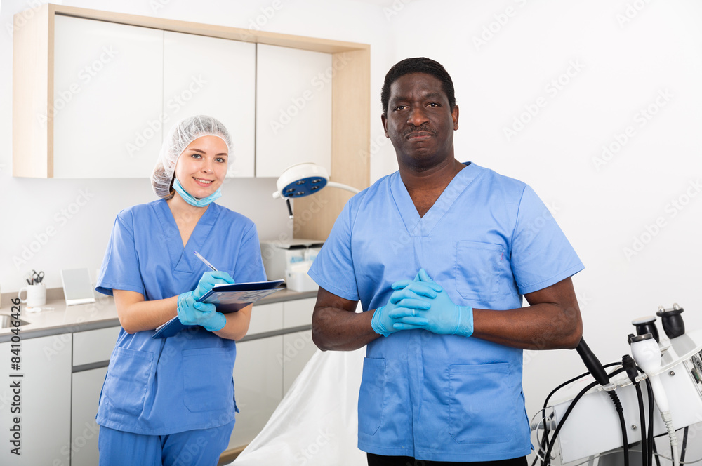 Obraz premium Two professional cosmetologists meeting patient in medical office, female doctor filling out medical form at clipboard