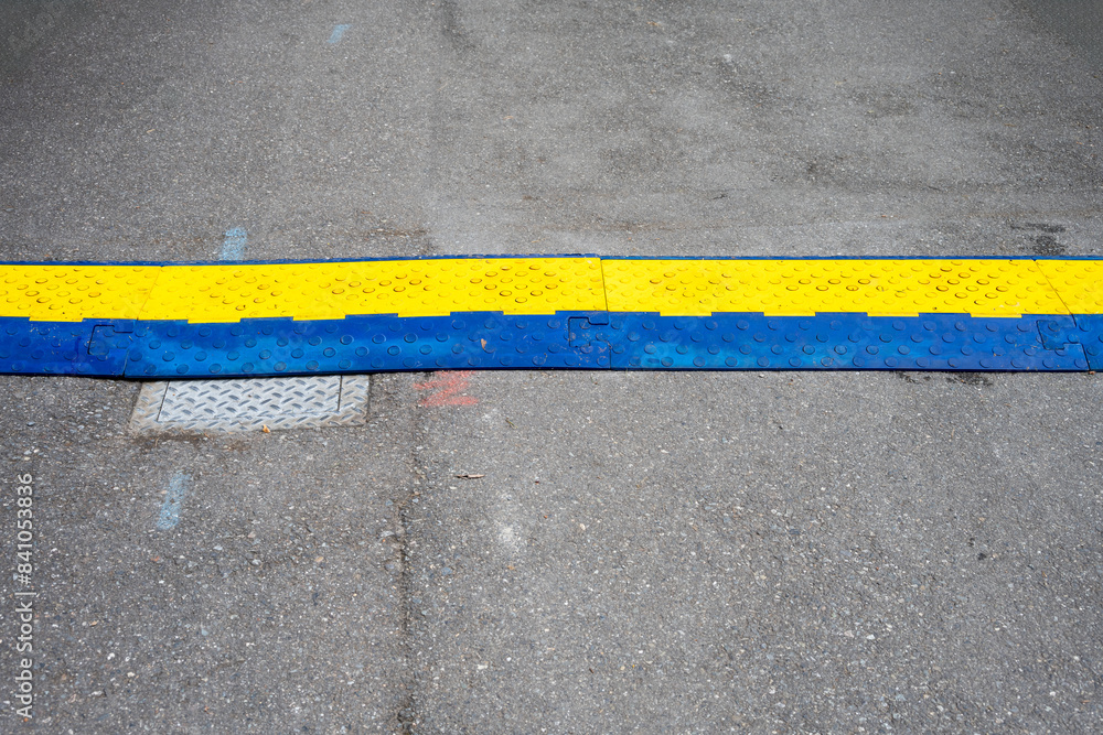 Fototapeta premium Blue and yellow heavy duty plastic cover protecting electrical cable crossing over an asphalt roadway in a park