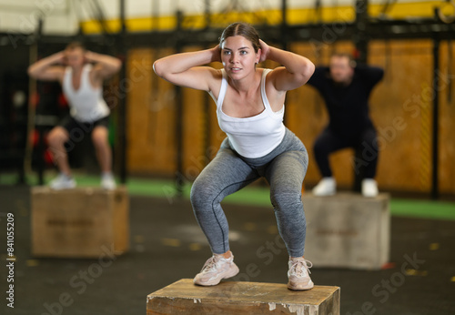 Active young girl squatting on box in sports hall during crossfit workout