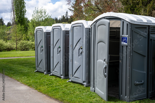 Setting up for a spring festival in a grass field in the park, portable bathrooms, including wheelchair accessible option, sunny day outside
