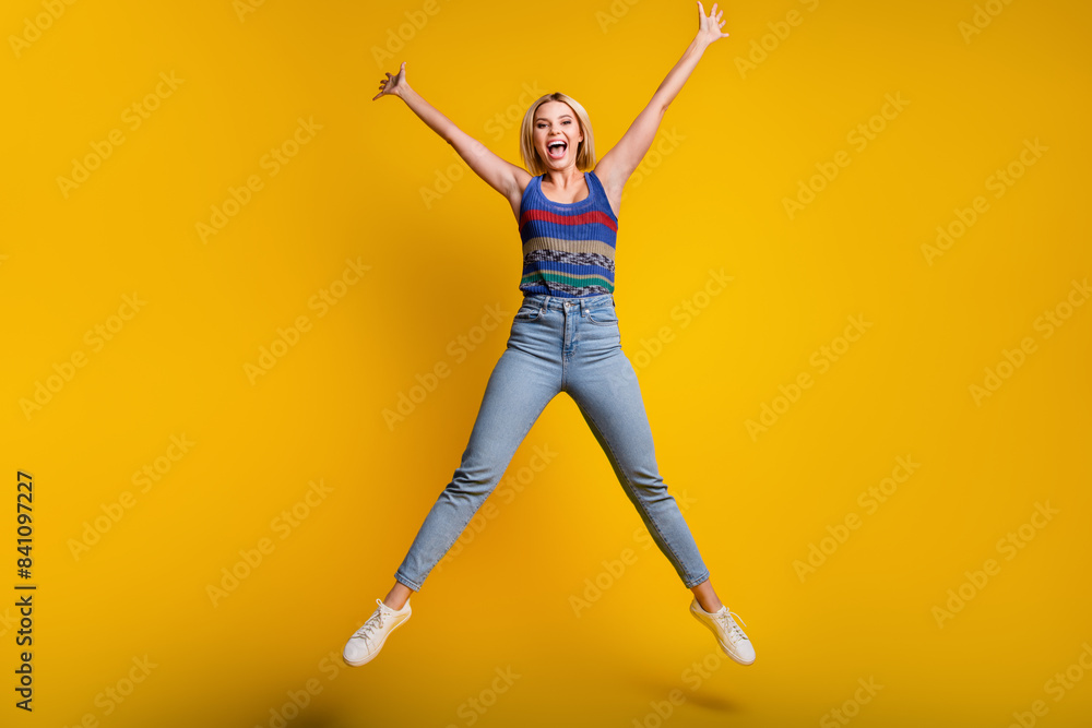Full body length photo of sportive funny jumping woman in jeans and singlet create star symbol with body isolated on yellow color background Full body length photo of sportive funny jumping woman in jeans and singlet create star symbol with body isolated on yellow color background