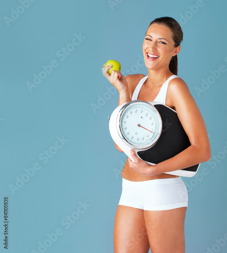 Woman  scale and apple for weight loss  portrait and nutrition on blue studio background. Healthy  wellness and excited for diet  mockup space and winner with victory  organic food or body positivity