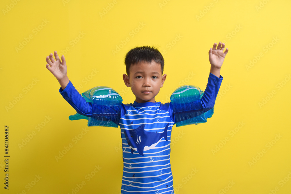 Portrait of a cute little Asian boy wearing a swimsuit posing with both hands raised isolated on a yellow background. Summer vacation concept. With Copy space Portrait of a cute little Asian boy wearing a swimsuit posing with both hands raised isolated on a yellow background. Summer vacation concept. With Copy space