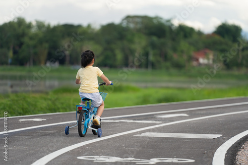 Back side view of asian baby girl child learning to ride bicycle in the park garden. Education concept for kid practiice cycling at park  baby sport concept.