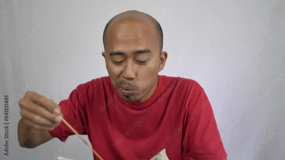 bald-headed adult Asian man eating chicken satay bald-headed adult Asian man eating chicken satay