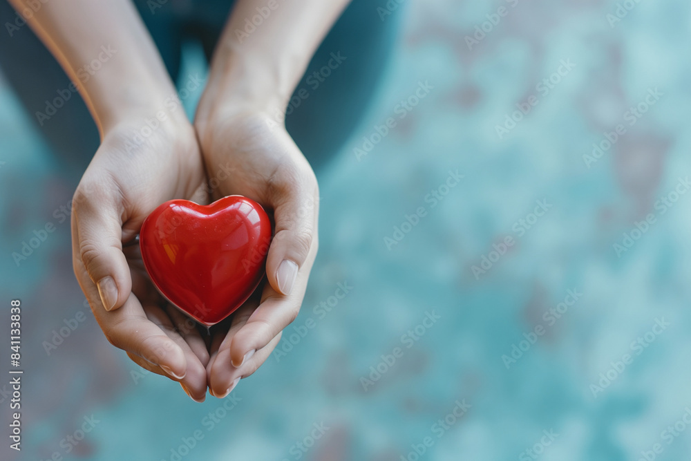 A woman is holding a red heart in her hand. The heart is made of rubber and is placed on a grey surface. Concept of love and warmth, as the woman is holding the heart with care and affection A woman is holding a red heart in her hand. The heart is made of rubber and is placed on a grey surface. Concept of love and warmth, as the woman is holding the heart with care and affection