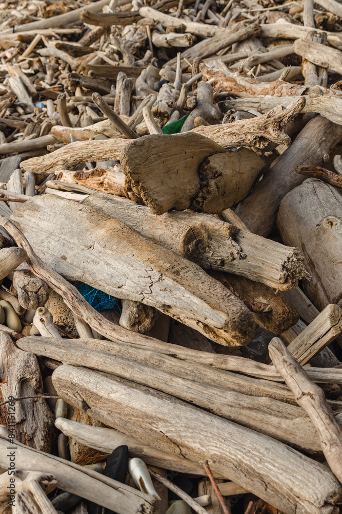 A pile of weathered pieces of driftwood, varying in size and shape, with small rocks and debris. Close-up of wooden rubbish on the seashore. A pile of weathered pieces of driftwood, varying in size and shape, with small rocks and debris. Close-up of wooden rubbish on the seashore.