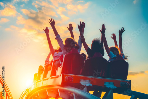 Fototapeta Naklejka Na Ścianę i Meble -  People cheering and enjoying a roller coaster ride at the amusement park with sunset in the background.