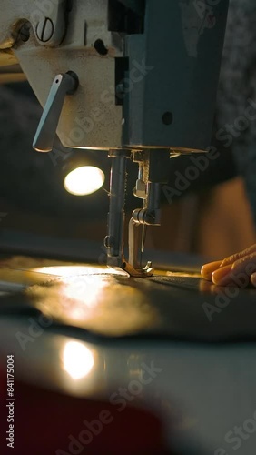 Working sewing machine presser foot, stitching in slow motion. Tailor's hand holding sewing leather carefully. Manufacturing individual leather bags, belts, accessories. Vertical shot.