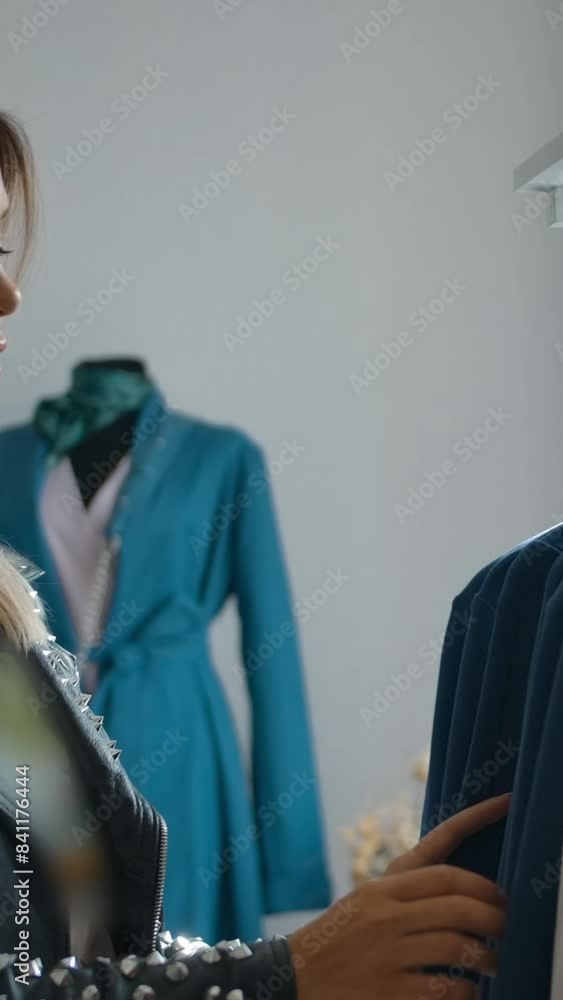 Young female in trendy outfit smiling and selecting new garment from clothes rail in slow motion while shopping in weekend. Vertical shot. Young female in trendy outfit smiling and selecting new garment from clothes rail in slow motion while shopping in weekend. Vertical shot.