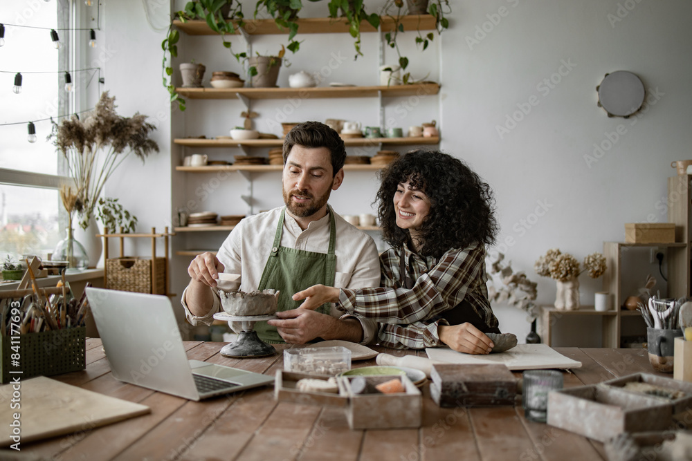 Fototapeta premium Bearded mature man and woman vlogger sculpt vases and bowls from clay in studio, recording content for online courses or social media.