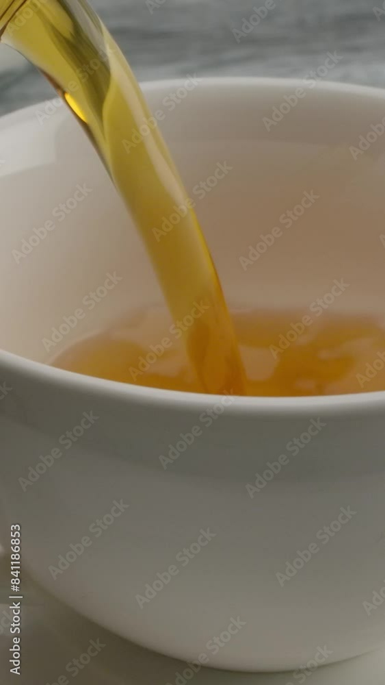 Pouring black tea into a classic white cup on a saucer from teapot. Dolly macro slow motion of red-brown golden tea. Vertical shot. Pouring black tea into a classic white cup on a saucer from teapot. Dolly macro slow motion of red-brown golden tea. Vertical shot.