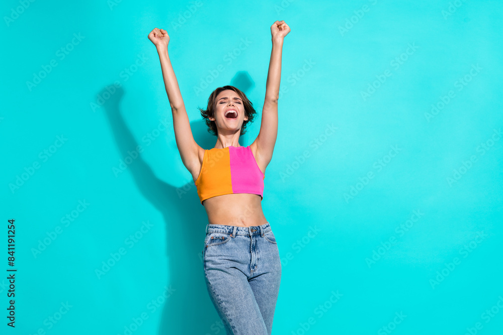 Photo of lucky cool woman wear pink orange top shouting yeah rising fists empty space isolated teal color background Photo of lucky cool woman wear pink orange top shouting yeah rising fists empty space isolated teal color background