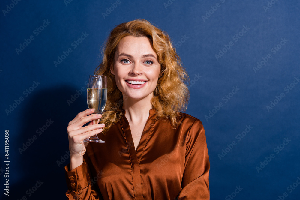 Photo of gorgeous cheerful girl with curly hairdo wear blouse holding champagne glass smiling isolated on dark blue color background Photo of gorgeous cheerful girl with curly hairdo wear blouse holding champagne glass smiling isolated on dark blue color background