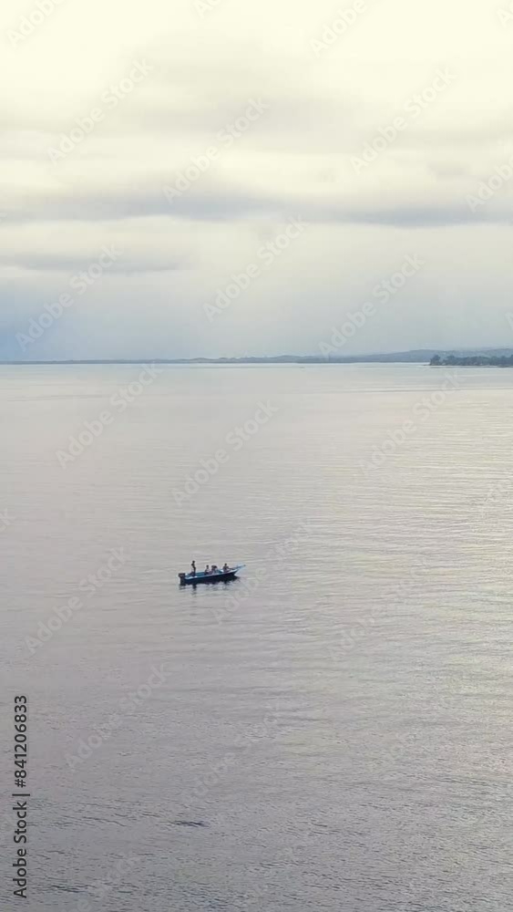 A serene view of a solitary boat floating on a calm sea under a cloudy sky, evoking a sense of tranquility. Vertical footage