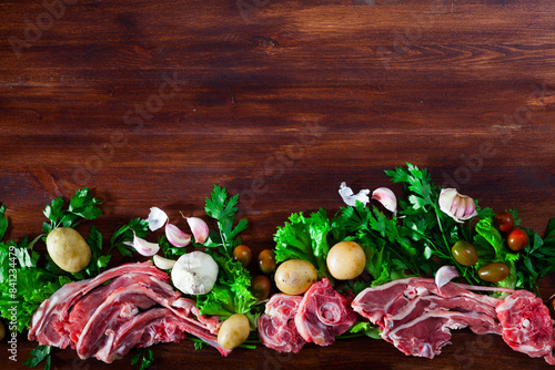 Raw lamb meat with fresh vegetables, greens and spices on wooden background.. photo