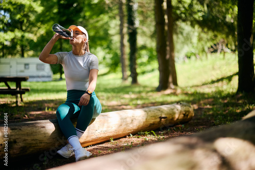 Quadro su tela Thirsty sportswoman drinking water from  bottle while exercising in nature