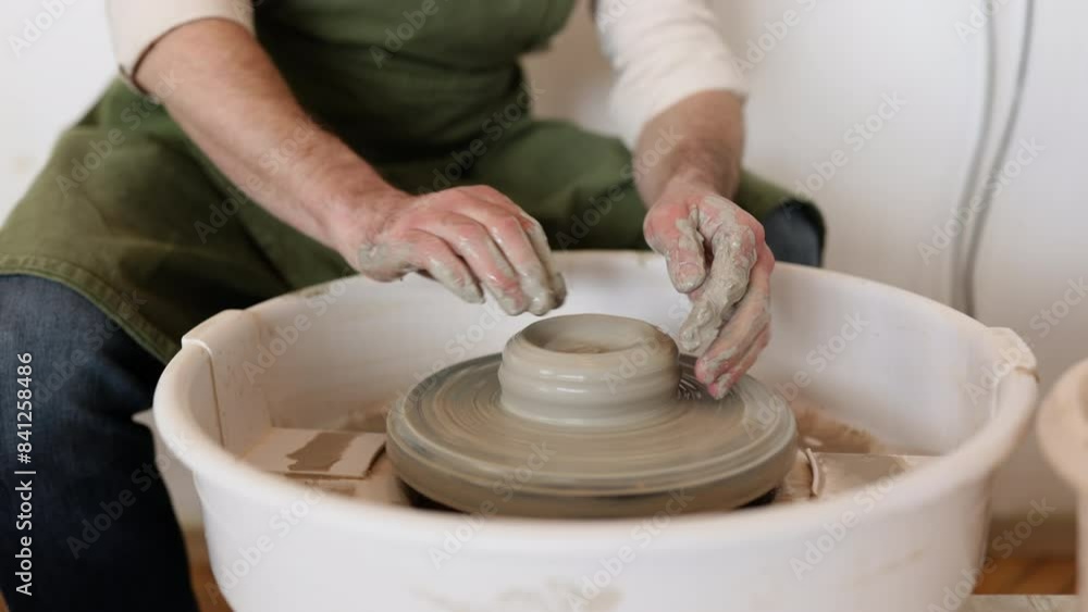 A male potter carefully sculpts a clay bowl with the help of a potter's wheel in a studio setting. A male potter carefully sculpts a clay bowl with the help of a potter's wheel in a studio setting.
