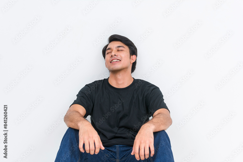Handsome young man feeling relieved while sitting and leaning against a wall Handsome young man feeling relieved while sitting and leaning against a wall