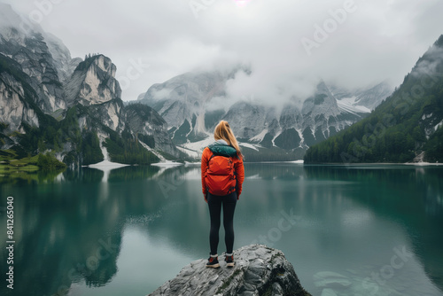 Mountain lake view. Female hiker with orange backpack. Serene nature scene.