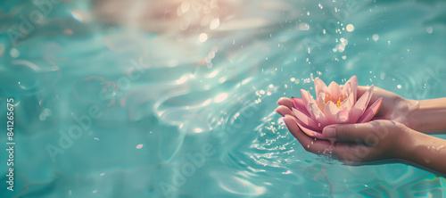 close up of hands holding a gentle pastel pink lotus flower with azzur water splash on a light blue background . Spa, yoga,meditation, calmness and relaxiation concept. Greeting card for Vesak day  photo