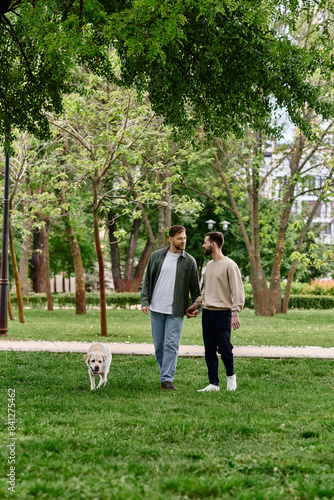 A bearded gay couple walks hand-in-hand through a verdant park with their labrador retriever.