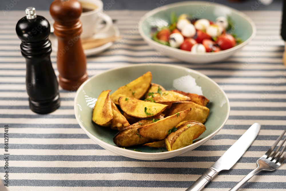 Fried potatoes and fresh vegetable salad for dinner served on a table with a striped tablecloth and cutlery Fried potatoes and fresh vegetable salad for dinner served on a table with a striped tablecloth and cutlery