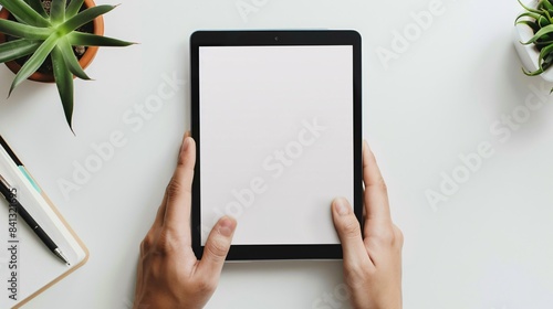 Close-up of hands holding a black tablet with a white screen on a white table