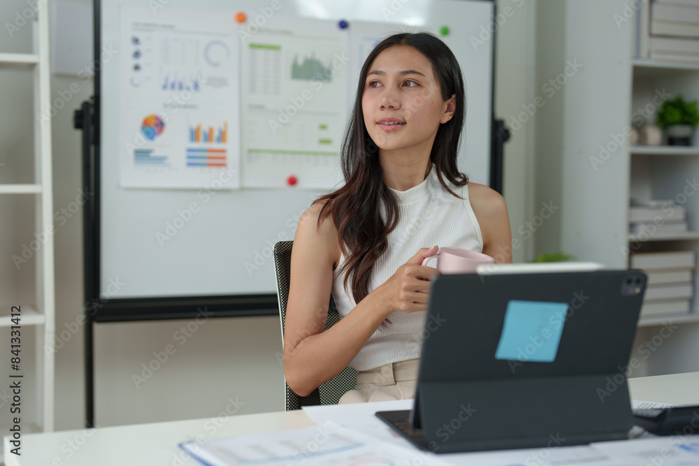 Young Asian woman working on laptop and drinking coffee in living room relaxing at home. Asian business woman working with financial documents Calculator, calculations, holiday concept at work. Young Asian woman working on laptop and drinking coffee in living room relaxing at home. Asian business woman working with financial documents Calculator, calculations, holiday concept at work.