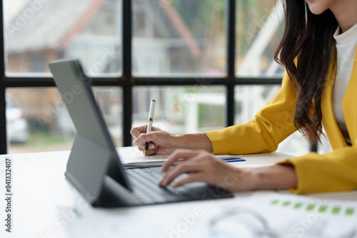 Asian businesswoman sitting at home office with glasses, laptop, financial documents online marketing Write down information, income, startup business ideas. © Phimwilai