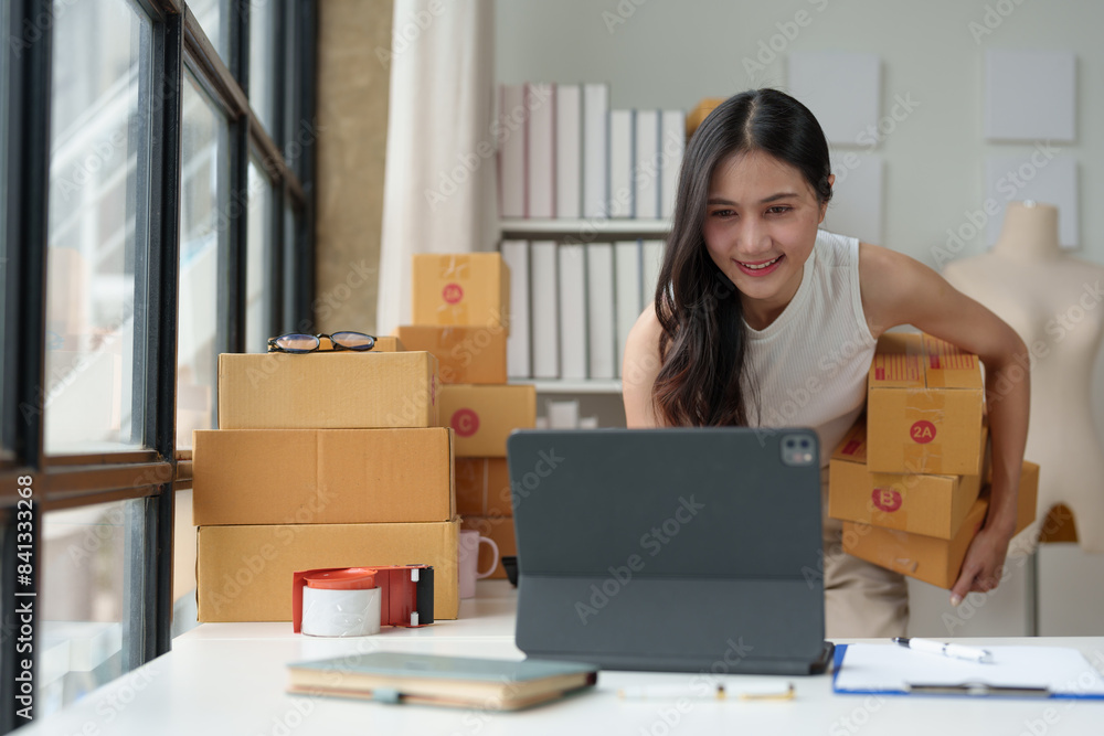 Small Business Entrepreneur SME Freelance Woman Working at Home Office Using Laptop for Checking Online Marketing, Packaging Boxes, SME Seller, Concepts, Ecommerce, Online Sales. Small Business Entrepreneur SME Freelance Woman Working at Home Office Using Laptop for Checking Online Marketing, Packaging Boxes, SME Seller, Concepts, Ecommerce, Online Sales.