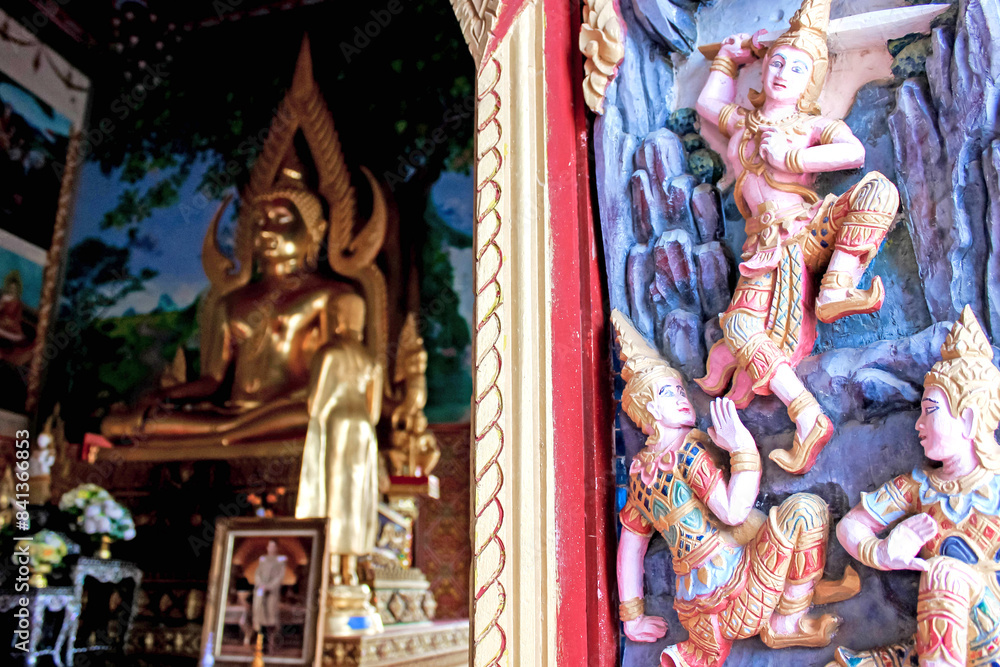 Obraz premium Thai temple has a Golden Buddha statue and intricate wall art, reflecting traditional beauty