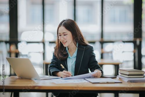 Young Asian professional business woman office worker analyst sitting at desk working on laptop thinking on project plan, analyzing marketing or financial data online, watching elearning webinar.