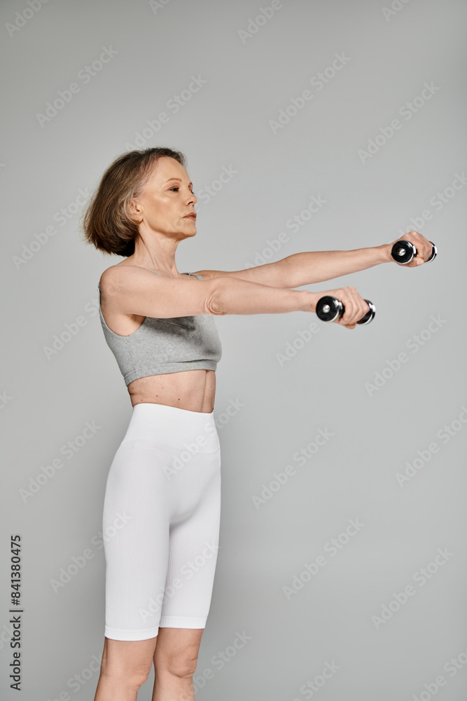 Attractive woman in active wear exercising with dumbbells on a gray background. Attractive woman in active wear exercising with dumbbells on a gray background.