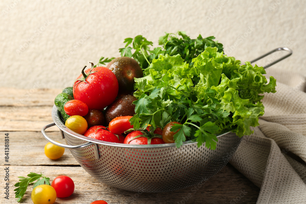 Wet vegetables in colander on wooden table, closeup Wet vegetables in colander on wooden table, closeup
