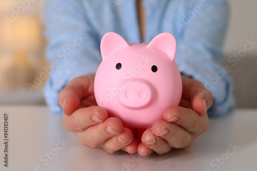Woman with pink piggy bank at white table  closeup
