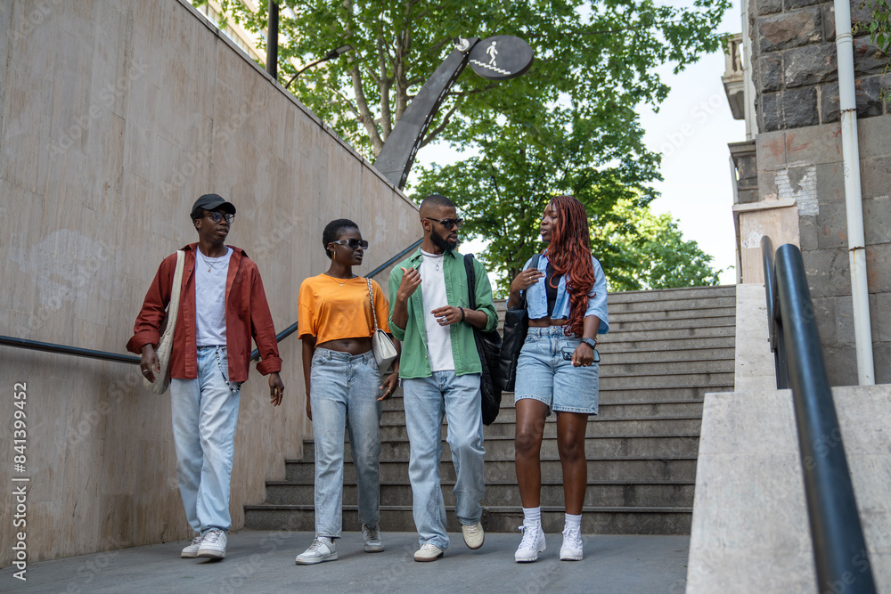 Obraz premium Group of stylish african american friends stroll through city streets, enter underpass, spend time with exciting conversations. Serious black students interested in dialogue communicate walks outside