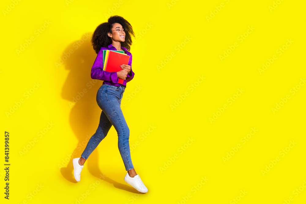 Full body photo of attractive young woman hold books running dressed stylish violet clothes isolated on yellow color background Full body photo of attractive young woman hold books running dressed stylish violet clothes isolated on yellow color background