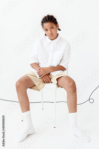 Stylish young boy sitting crosslegged on chair in white shirt and shorts, exuding trendy vibes photo